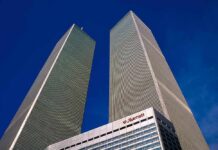 Twin rectangular skyscrapers rising above a hotel facade against a clear blue sky