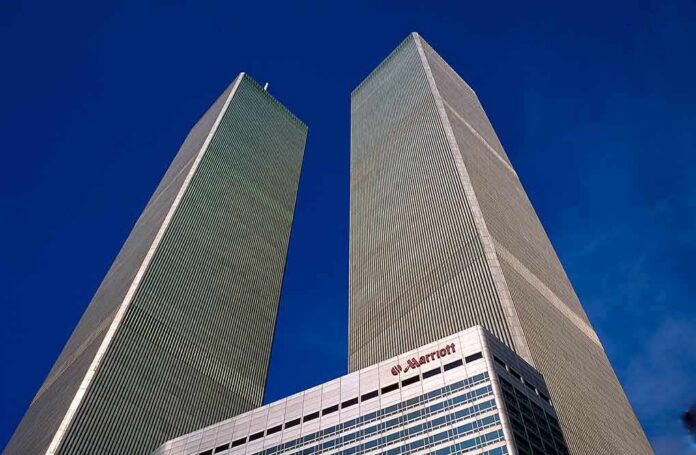 Twin rectangular skyscrapers rising above a hotel facade against a clear blue sky