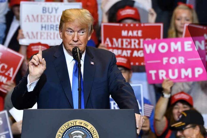 Donald Trump speaking at a rally podium with crowd holding signs