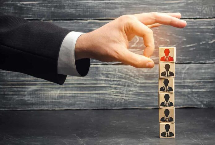 Hand selecting a top block with a red figure from a stack of employee icons