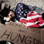 Homeless man sleeping on cardboard under an American flag