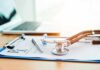 Stethoscope on a prescription form beside a pen and laptop