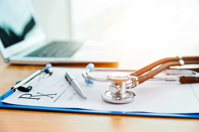Stethoscope on a prescription form beside a pen and laptop