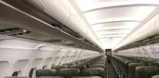 Airplane cabin with empty rows of economy seats and overhead bins