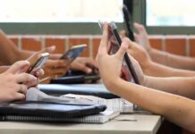 students' hands using smartphones at a classroom table