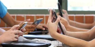 students' hands using smartphones at a classroom table