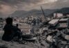 Boy sitting on rubble overlooking a devastated city