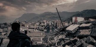 Boy sitting on rubble overlooking a devastated city