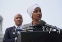 Ilhan Omar speaking at a podium with André Carson standing behind