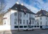 White embassy building with flag and parked cars on city street