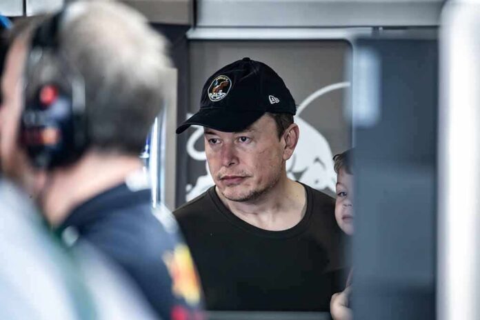 Elon Musk wearing a black cap in a crowded indoor setting