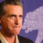 Gavin Newsom at a press event with a purple backdrop