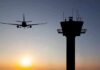 Airplane approaching runway near airport control tower at sunset