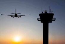 Airplane approaching runway near airport control tower at sunset