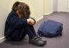 Norway’s Power Play: Seized Over Spanking Fears Child sitting on hallway floor with head down beside backpack