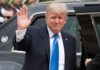 Donald Trump waves while standing beside a black vehicle