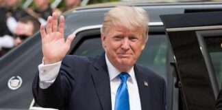 Donald Trump waves while standing beside a black vehicle